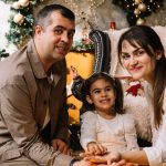 A man and a woman sitting next to a little girl in front of a christmas