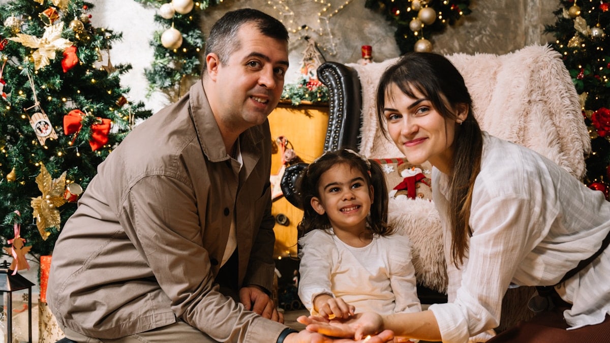 A man and a woman sitting next to a little girl in front of a christmas