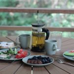 Casual breakfast with berries, veggies, and tea on a wooden porch table.