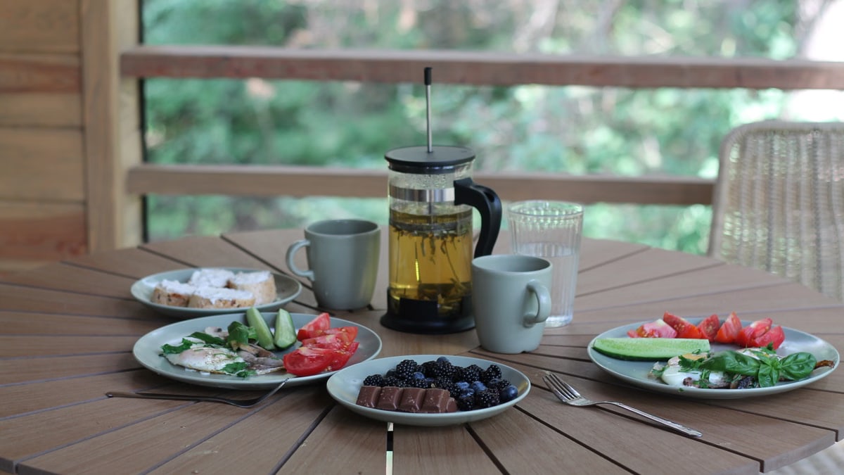 Casual breakfast with berries, veggies, and tea on a wooden porch table.